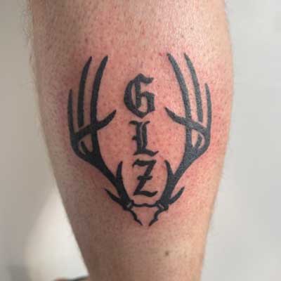 Antlers and initials memorial tattoo on a leg