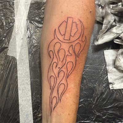 A tattoo of a Harley Davidson logo with flames on a forearm