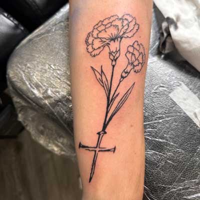 A carnation and cross tattoo on the back side of a forearm